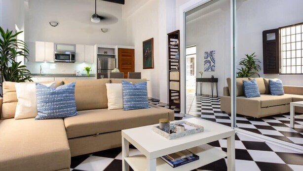 Uma sala de estar moderna com sofá, mesa de centro e cozinha ao fundo.