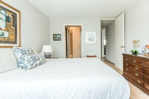 Een slaapkamer met een groot bed, een dressoir, een nachtkastje en een ingelijst beeld aan de muur.