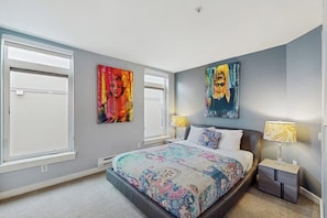 A bedroom with a bed, two paintings, a window, a nightstand, and a lamp. - Charming top floor 2 story penthouse with Sound and Olympic views (Seattle)