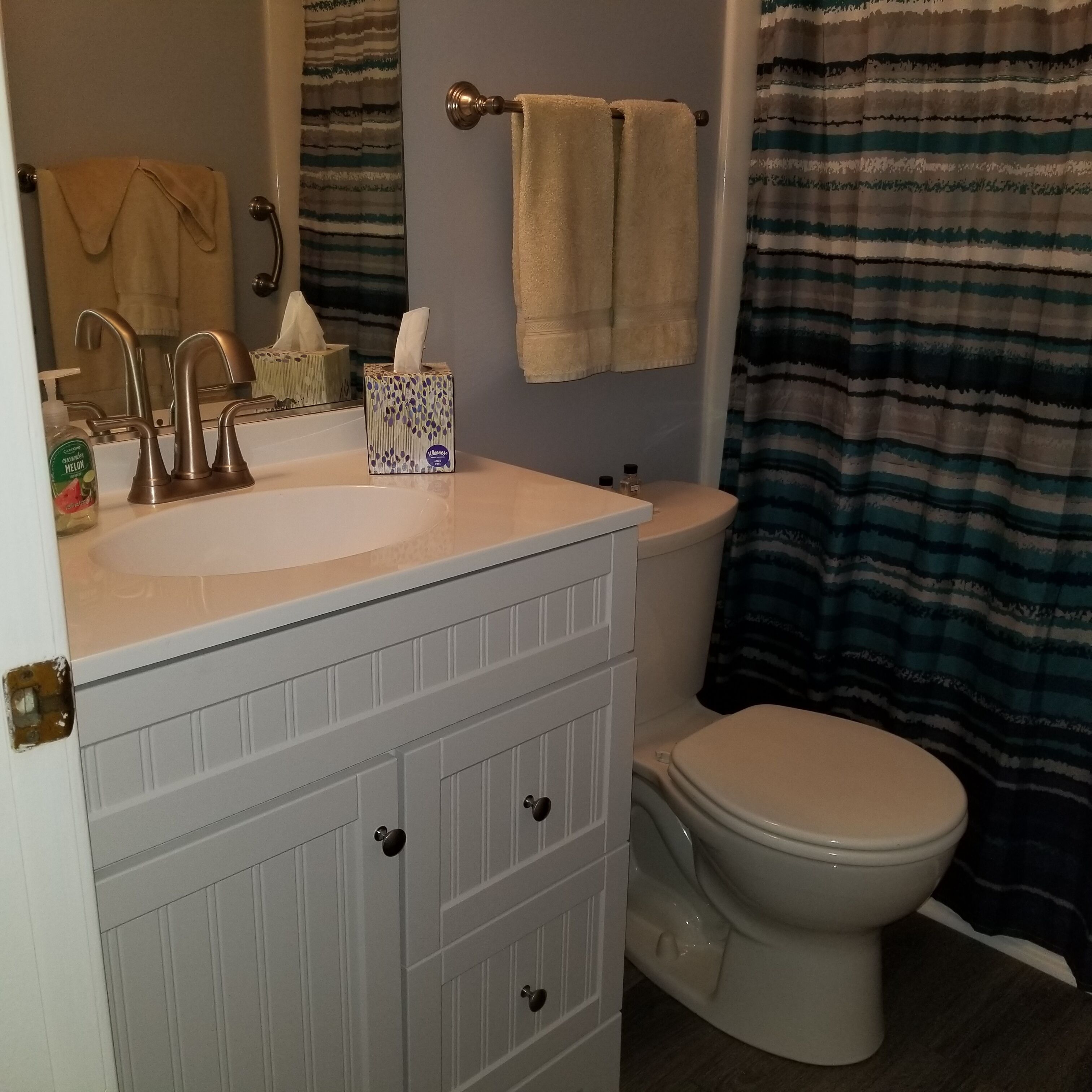 A bathroom with a white sink, a mirror, a toilet, and a striped shower curtain.