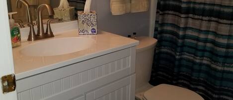 A bathroom with a white sink, a mirror, a toilet, and a striped shower curtain.