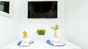 A white dining table with two chairs, a flat-screen TV mounted above, and a small potted plant on the table. - Azure Suite | 1 BR Apt at Old San Juan (San Juan)