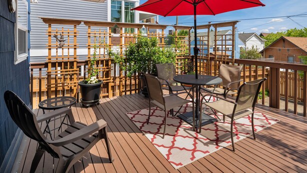 Eine Holzterrasse mit Gartenmöbeln, darunter ein Tisch und Stühle, sowie ein roter Sonnenschirm.