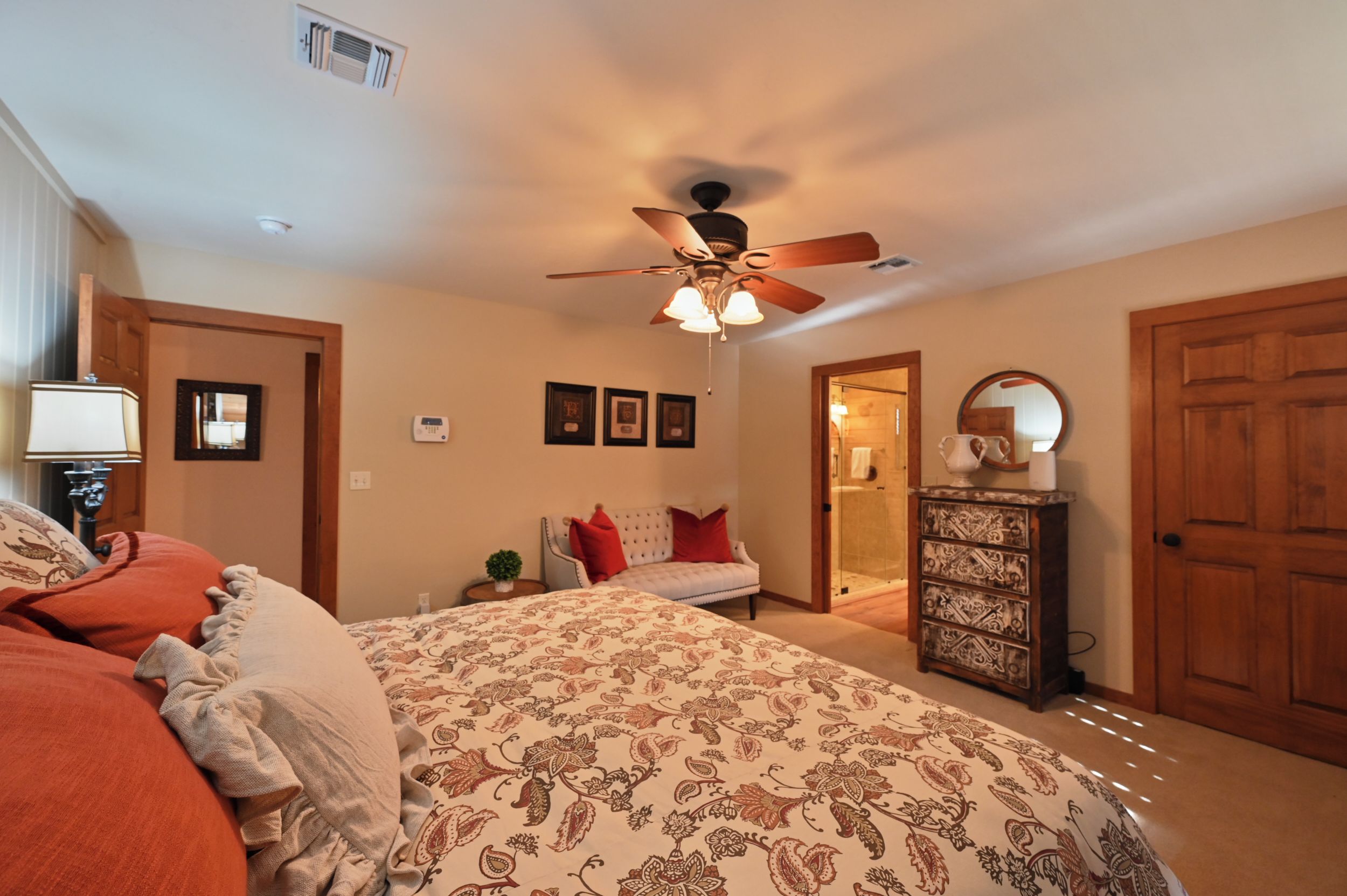 Une chambre à coucher comprenant un lit, un ventilateur de plafond, une commode et une porte donnant sur une autre pièce.