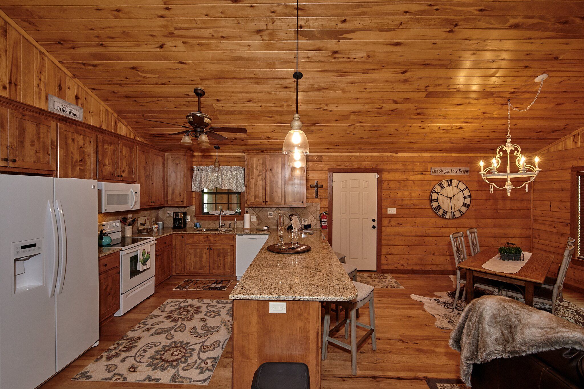 A cozy cabin-style kitchen with wooden walls, a central island, and a dining area with a chandelier.