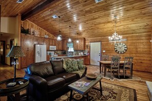 A cozy cabin interior with a wooden ceiling, a leather sofa, a dining table with chairs, and a chandelier. - Gateway Gathering - Cabin I Fredericksburg, stargazing (Fredericksburg)