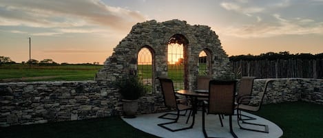Una estructura de piedra con ventanas en arco y una mesa con sillas en un jardín.