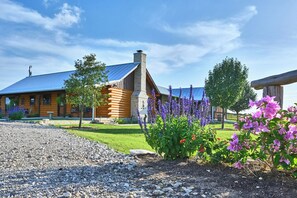 Eine rustikale Lodge mit auffälligem Schornstein, Holzbalkenbauweise und einem gepflegten Garten mit violetten Blumen und einem Kiesweg.