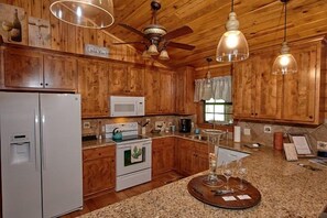 A wooden kitchen with a refrigerator, microwave, stove, and hanging lights.