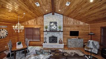 A cozy log cabin interior with a dining area, fireplace, leather sofa, and a chandelier.