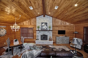 Un acogedor interior de cabaña de madera con comedor, chimenea, sofá de cuero y una araña.