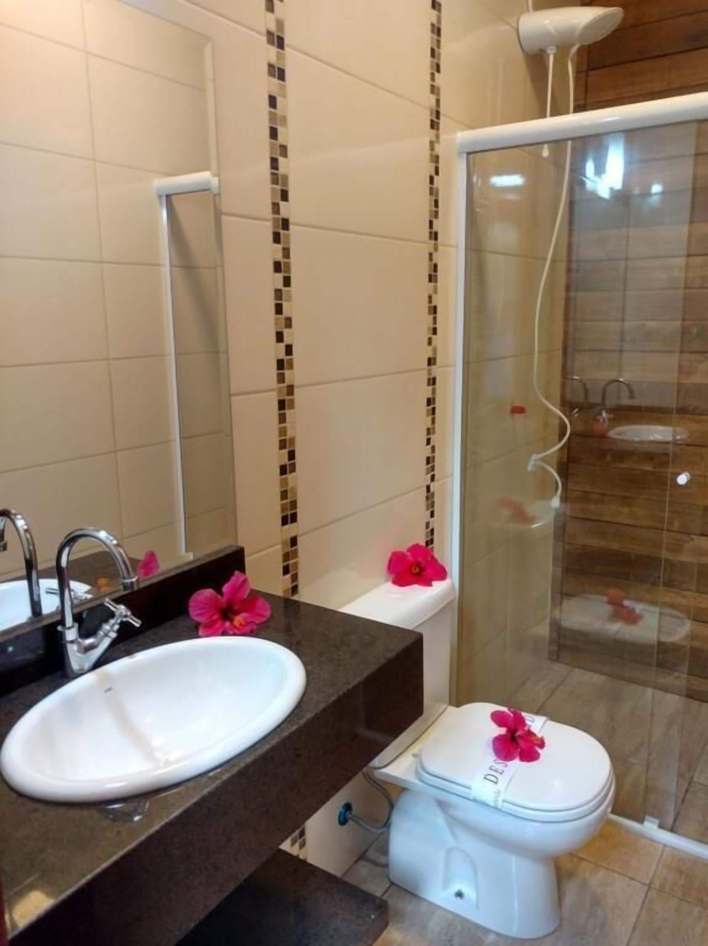 A bathroom with a white sink, a mirror, a toilet, and a shower area.