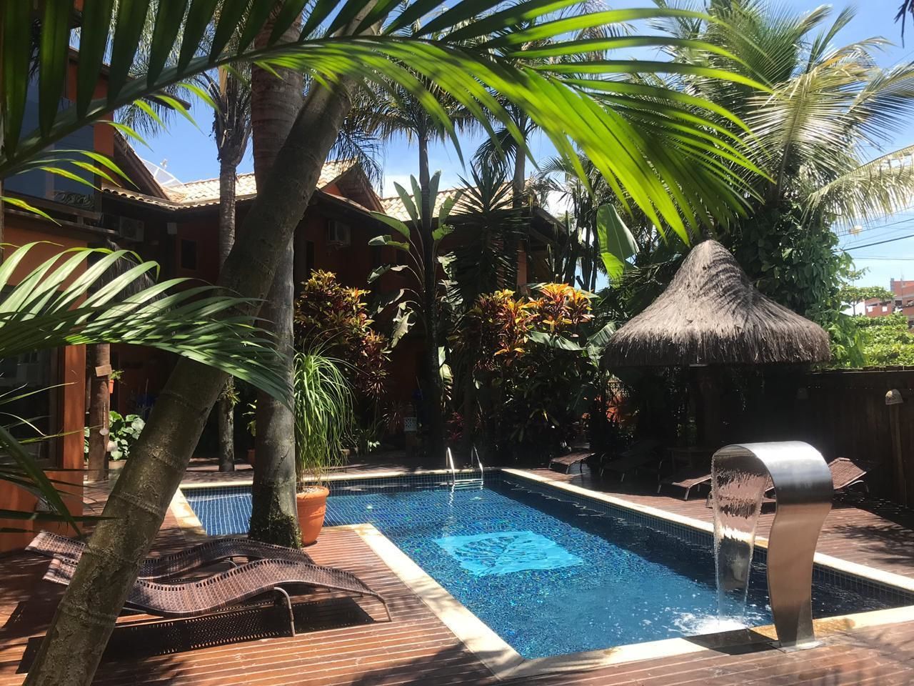 Una piscina con una estructura de techo de paja, rodeada de palmeras y plantas en macetas.