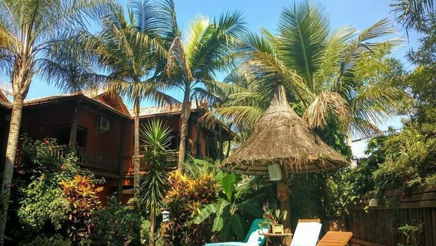 A pool area with lounge chairs, a thatched-roof structure, and tropical vegetation.