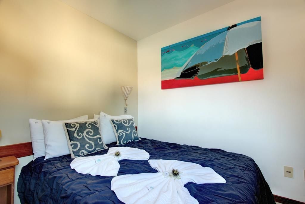 A hotel room with a large bed, a painting on the wall, and a nightstand.