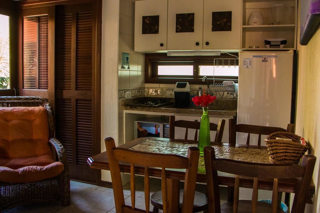 A compact kitchen with a dining area, featuring a table with chairs, a wicker chair, and a refrigerator.