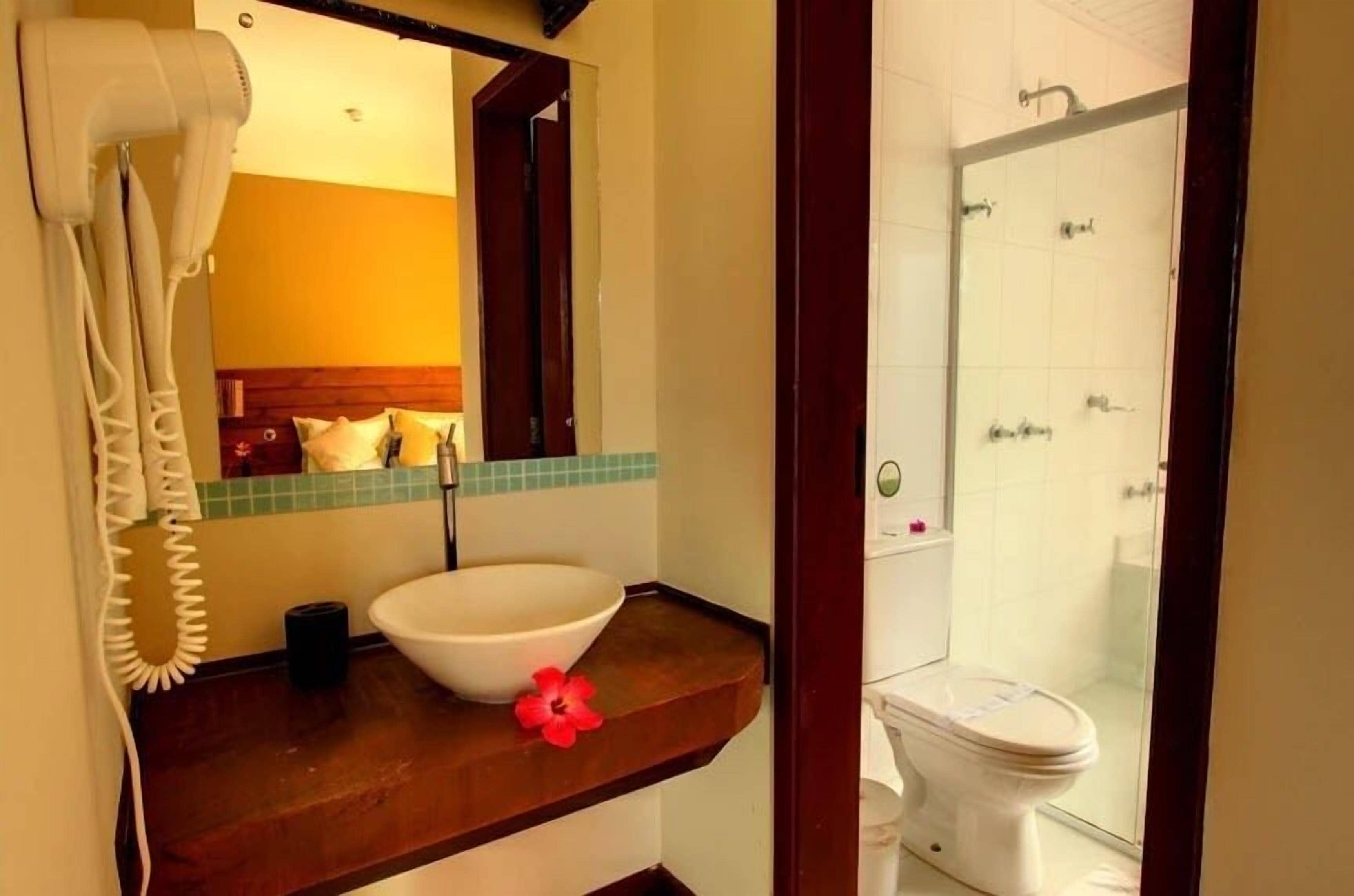 A bathroom with a wooden vanity, a white sink, a mirror, a hairdryer, and a shower area.
