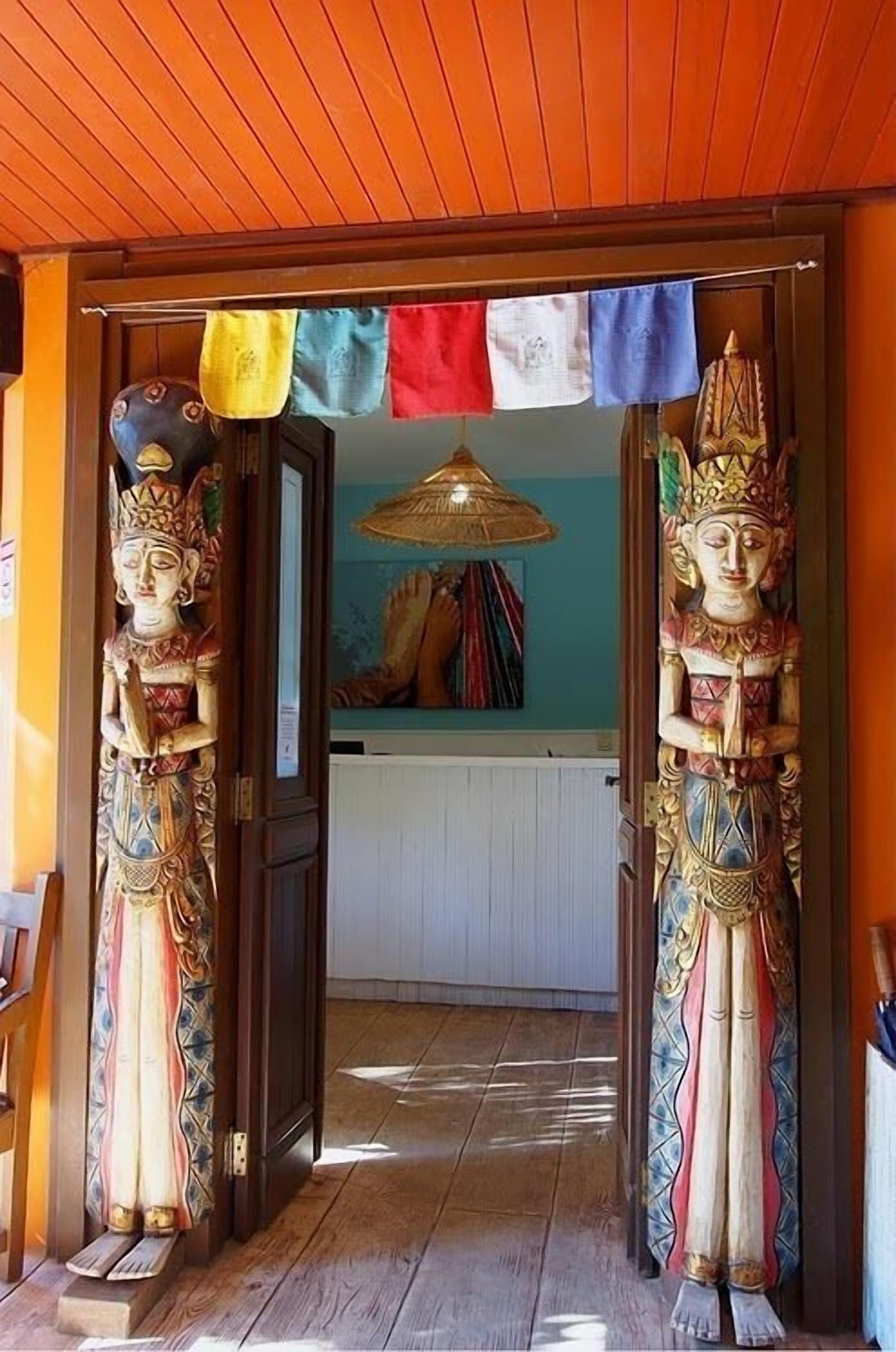 A doorway with two ornate statues on either side, leading into a room with a blue wall and a hanging basket.