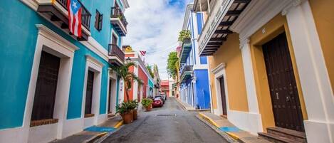 A narrow street lined with colorful buildings, each with balconies and potted plants.