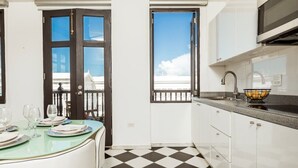 Una cocina moderna con armarios blancos, piso a cuadros blanco y negro, y un comedor con mesa y sillas de vidrio.