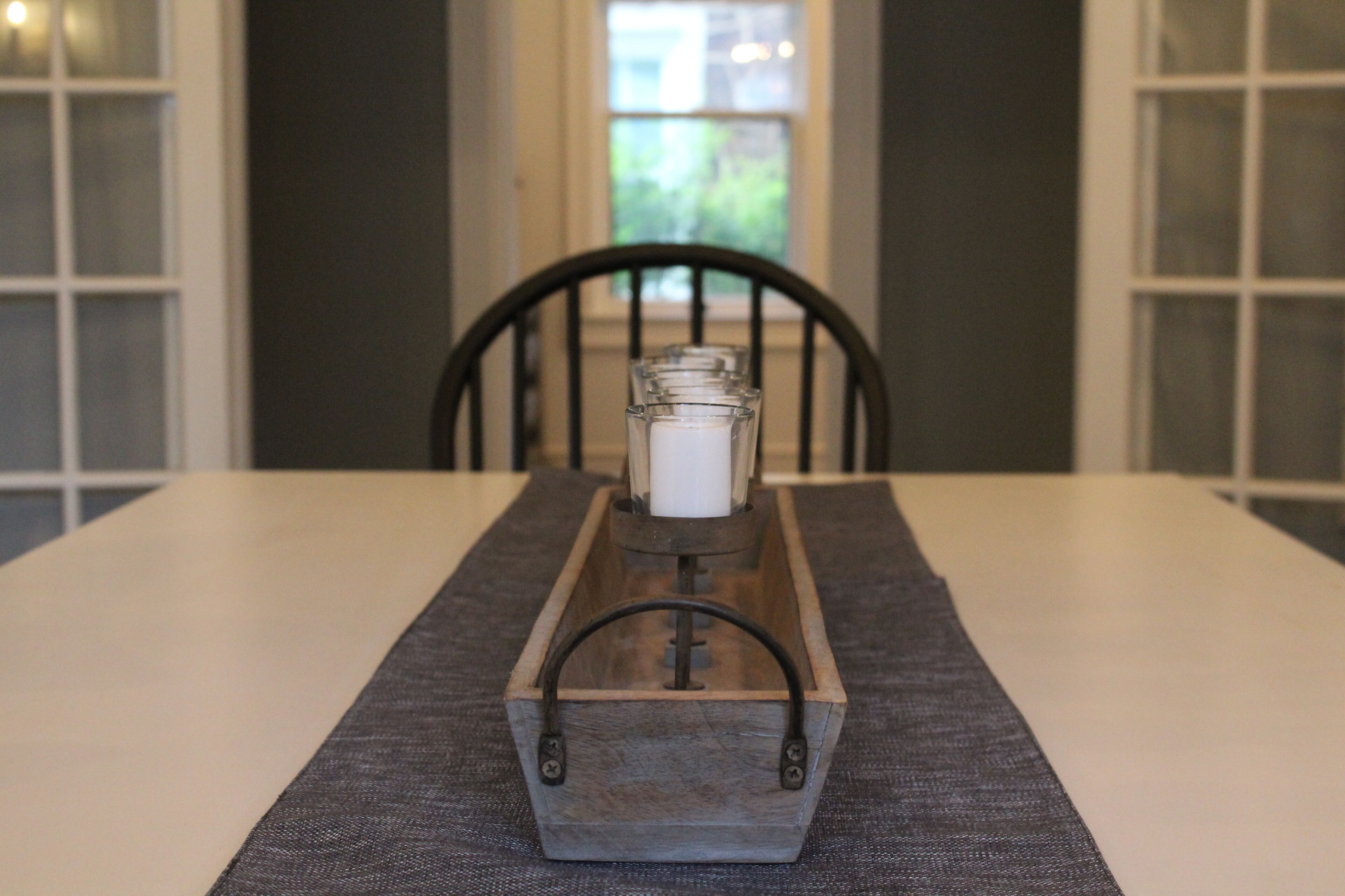 Una bandeja de madera con un portavelas sobre una mesa con un posavasos gris.