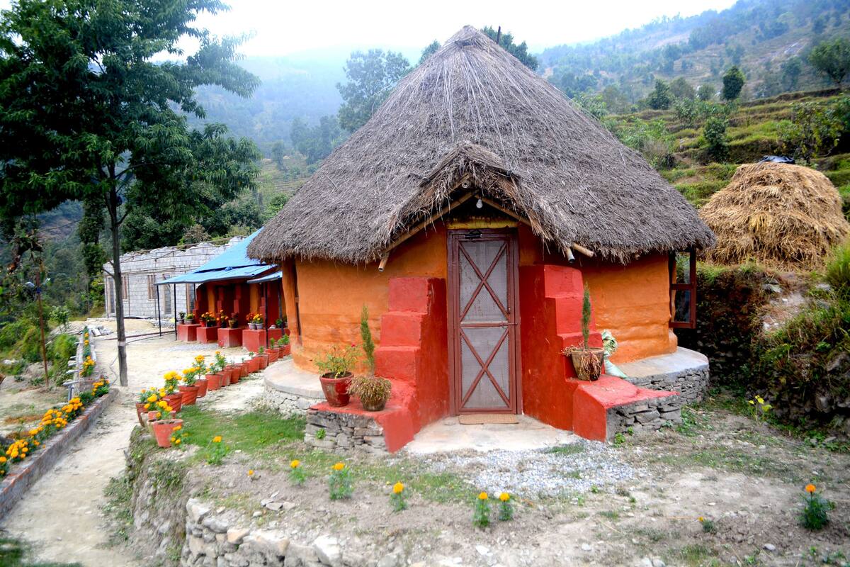 A thatched-roof house with a red door and a small porch area.