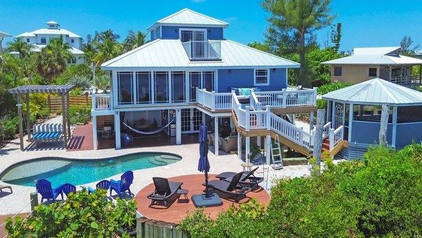 Una casa grande con piscina, mobiliario exterior y un patio cubierto.