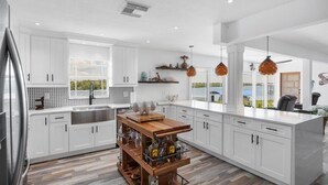 Una cocina moderna con armarios blancos, una isla de madera con utensilios de bar y grandes ventanas con vista al agua.
