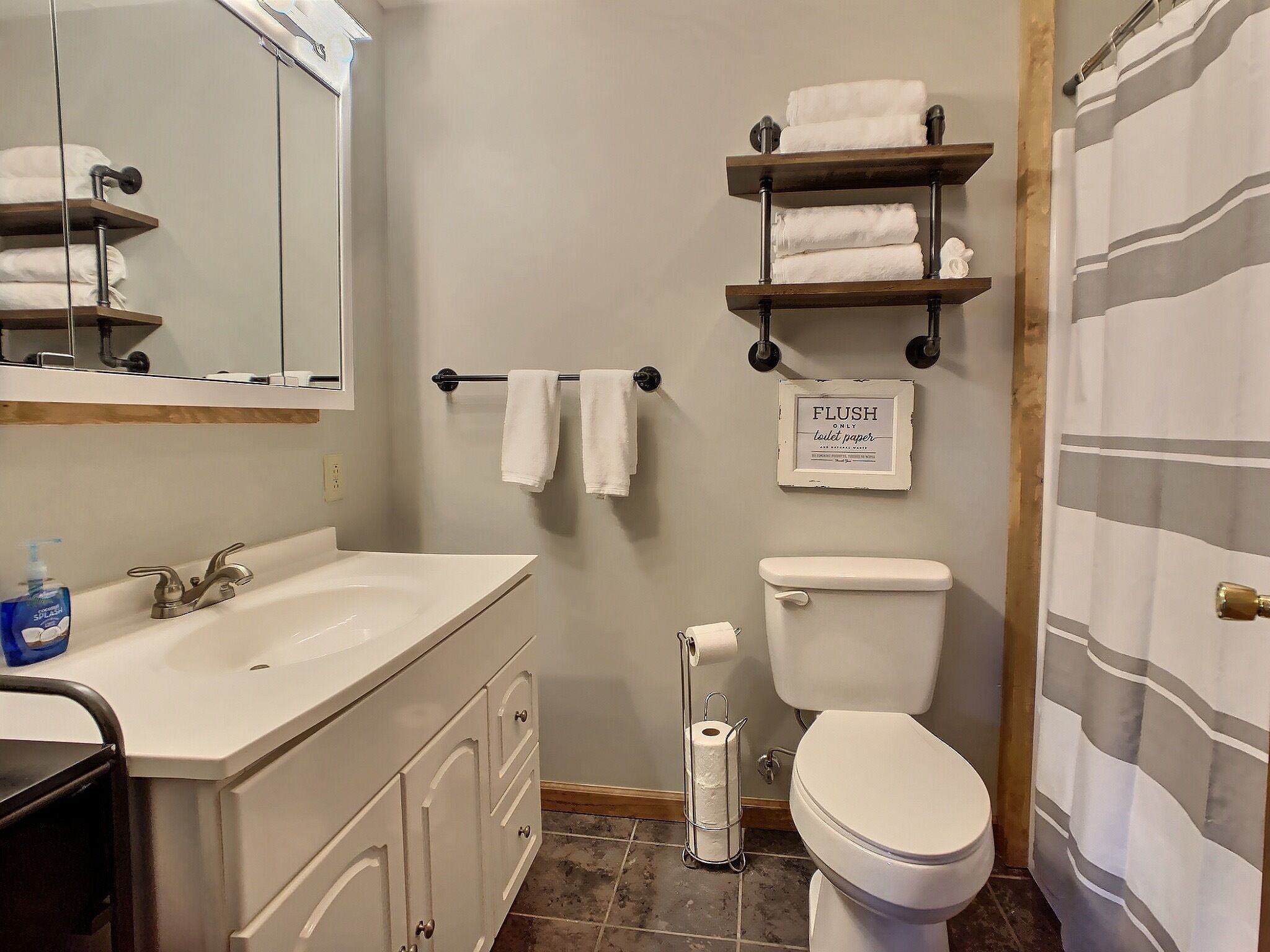 A bathroom with a white sink, a toilet, a shower curtain, and shelves with towels.