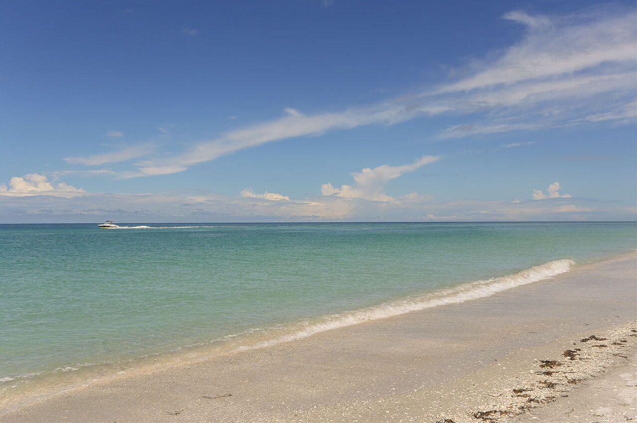 Une plage avec une eau turquoise et limpide, et un bateau visible au loin.