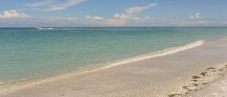 Une plage avec une eau turquoise et limpide, et un bateau visible au loin.