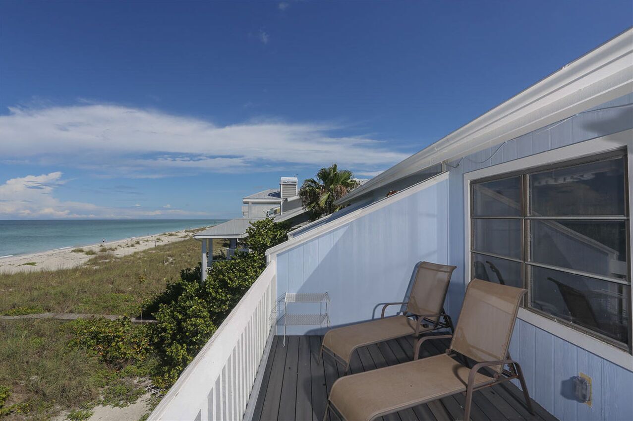 A balcony with two chairs overlooking a beach and ocean.