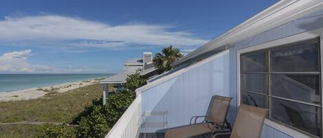 A balcony with two chairs overlooking a beach and ocean.