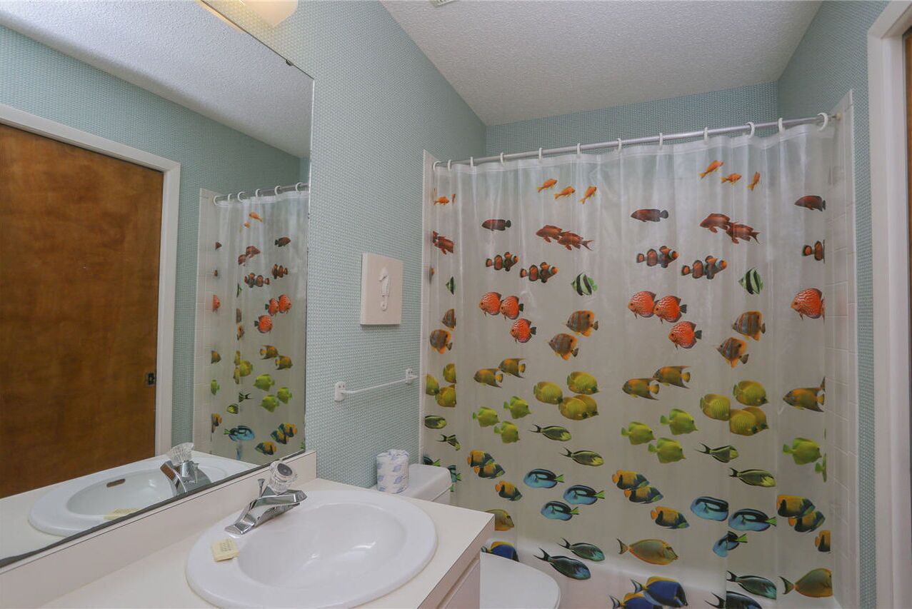 A bathroom with a white sink, a mirror, and a shower curtain with fish patterns.