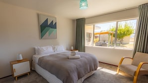 A bedroom with a large bed, a chair, a nightstand, a lamp, a painting, and a window with a view of the outside. - Rejuvenate on Rata · Rejuvenate on Rata, Twizel FREE WIFI (Twizel)