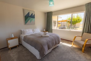 Um quarto com uma cama grande, uma cadeira, uma mesinha de cabeceira, uma luminária, um quadro e uma janela com vista para o exterior.