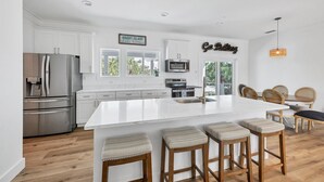 A modern kitchen with white cabinetry, stainless steel appliances, and a large island with bar stools. - Family Tides: Beach Pool and Dock..This 5 Bedroom beach house has it all! (Placida)