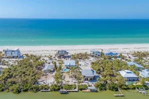 An aerial view of a coastal residential area with multiple houses, a beach, and a marina.