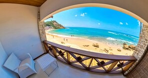 A balcony with a curved view of a beach, a small table, and a chair.