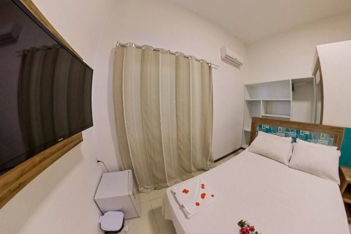 Ett hotellrum med en säng, en TV, ett litet skrivbord, en toalett och en duschdraperi.