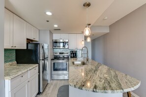 A modern kitchen with white cabinets, stainless steel appliances, a granite countertop, and pendant lighting. - Beachfront Condo in Panama City Beach with Sunset Views • Pools • Beach Service (Panama City Beach)