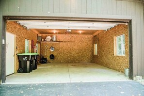 A garage with a concrete floor, wooden walls, and a metal roof. There are three trash bins and a bicycle rack.