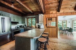 A kitchen with wooden cabinets, a large island with stools, and a dining area with chairs and a table.