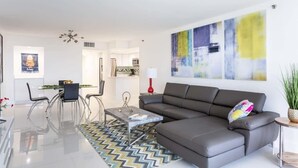 A modern living room with a grey sofa, a glass coffee table, and a dining area with a table and chairs.