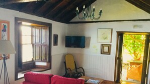 A cozy living room with a red sofa, a wooden chair, a television mounted on the wall, and a door leading to a garden.