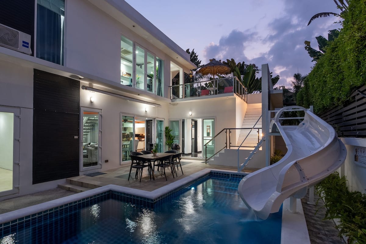 Une maison moderne à deux étages, dotée d’une piscine, d’un toboggan et d’un espace repas.
