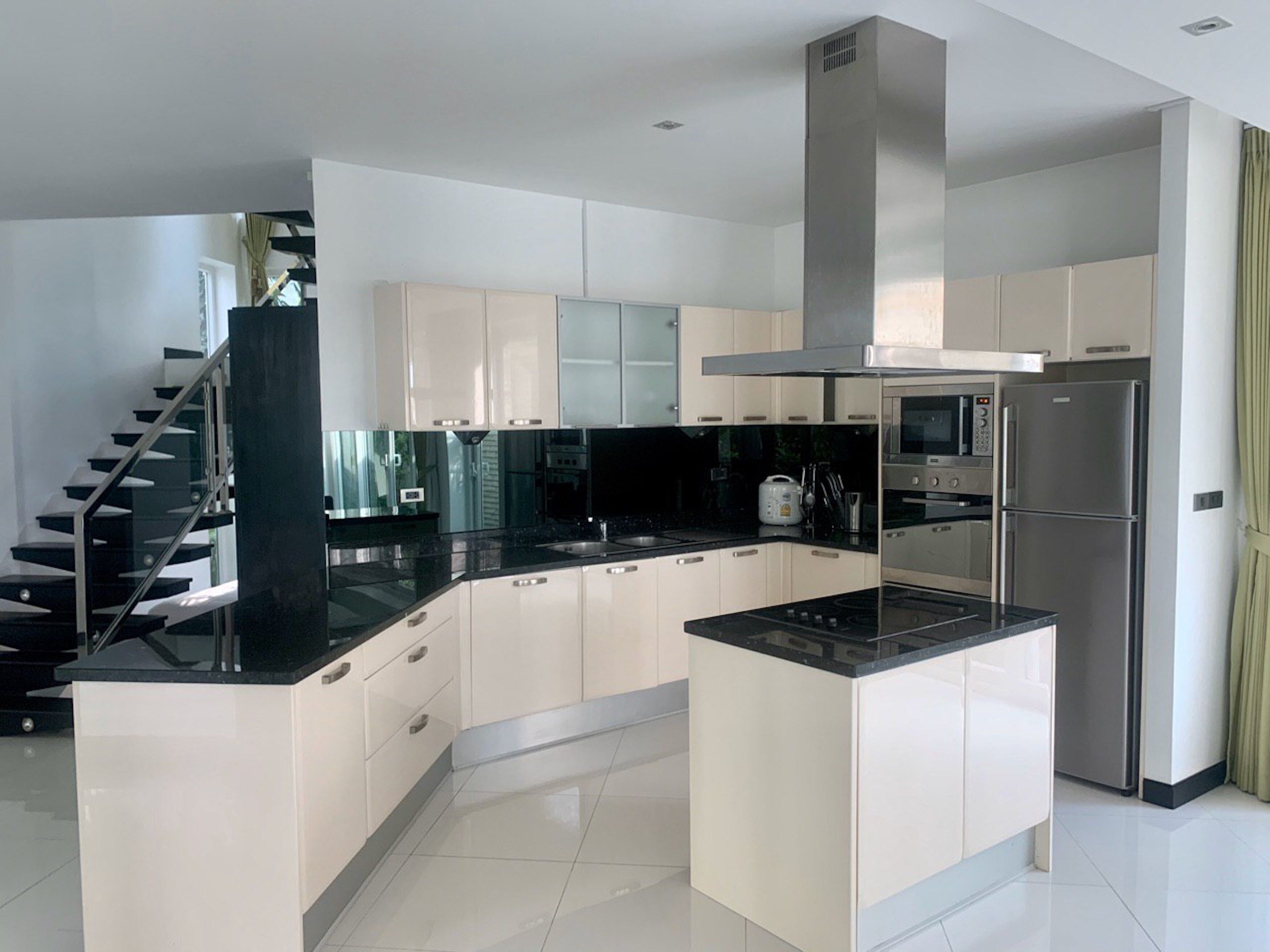 A modern kitchen with white cabinets, black countertops, stainless steel appliances, and a central island.