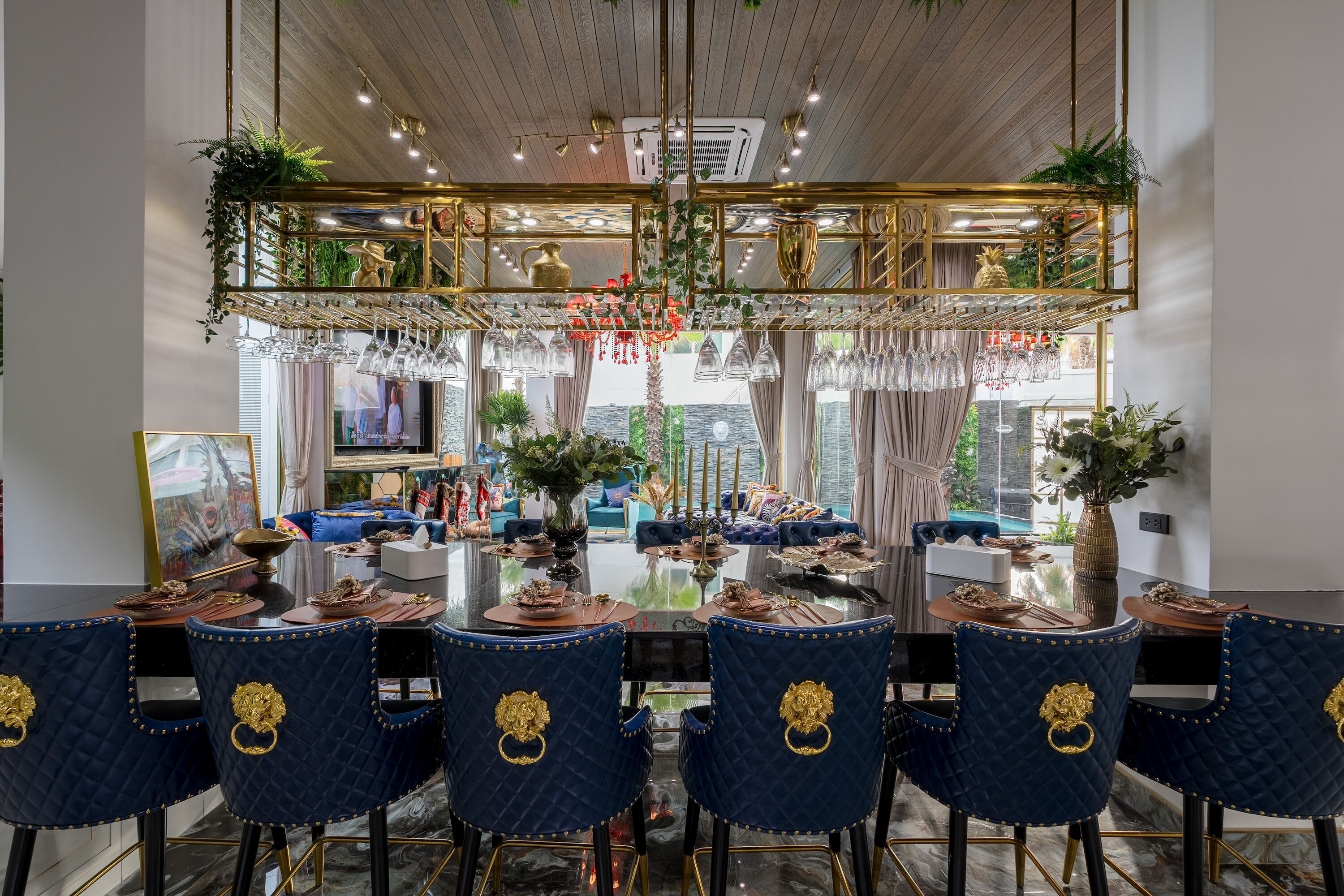 Ein Essbereich mit einem Glastisch, blau gepolsterten Stühlen mit goldenen Akzenten und einer Chandelüster.
