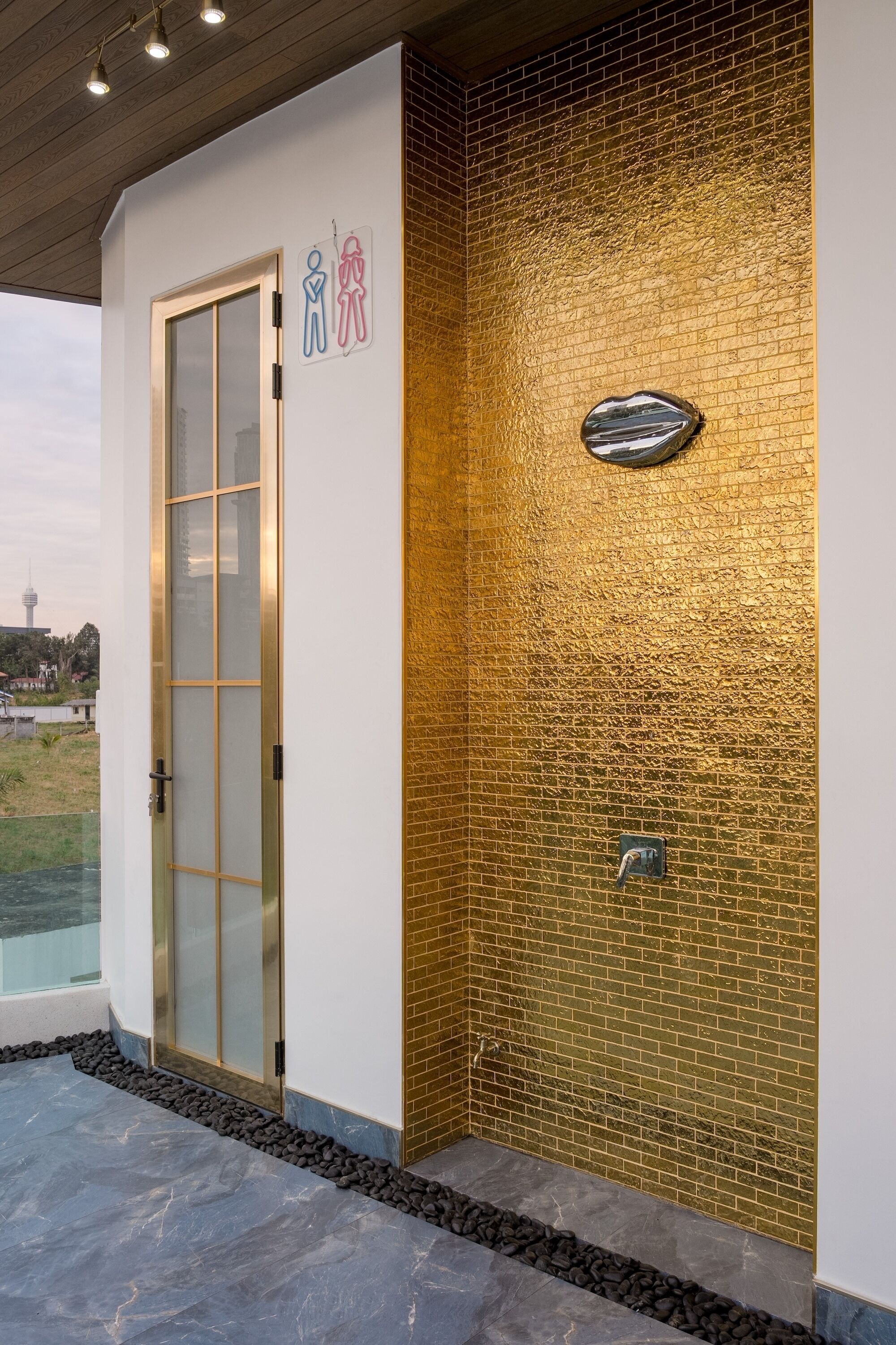 A building entrance with a glass door, a brick wall with a textured pattern, and a metal plaque.