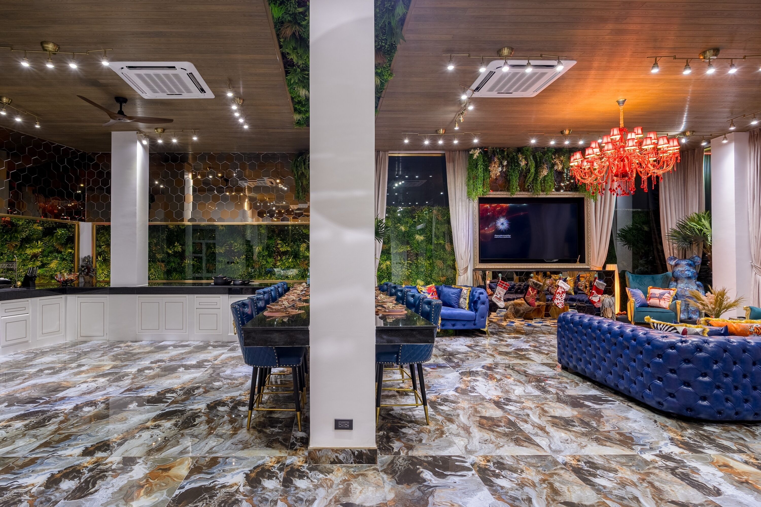 A luxurious indoor space with a marble floor, a large dining table, blue upholstered seating, a chandelier, and a large TV screen.